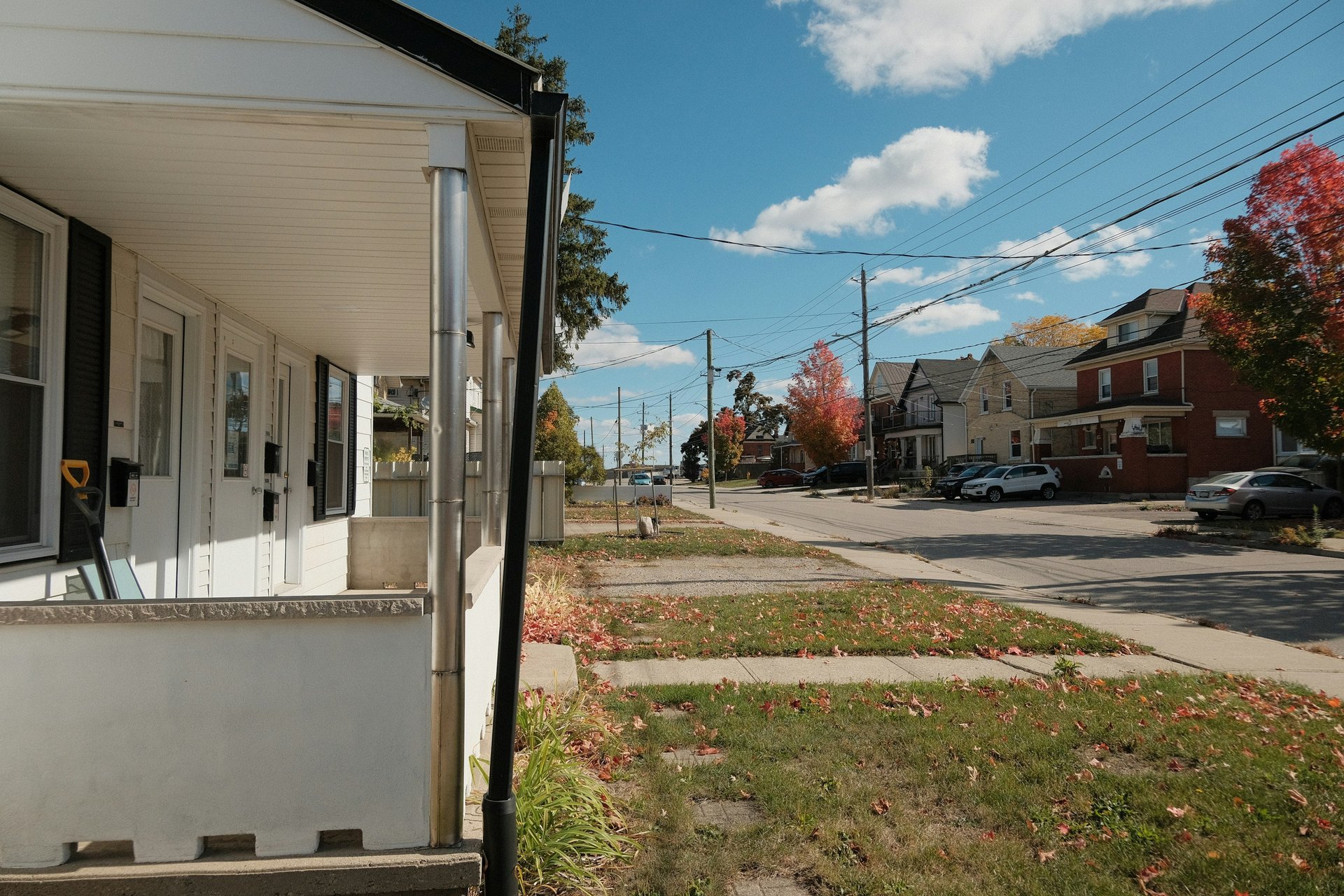 Covered porch with several white doors and mailboxes on a multi-unit house, beside a residential street in autumn