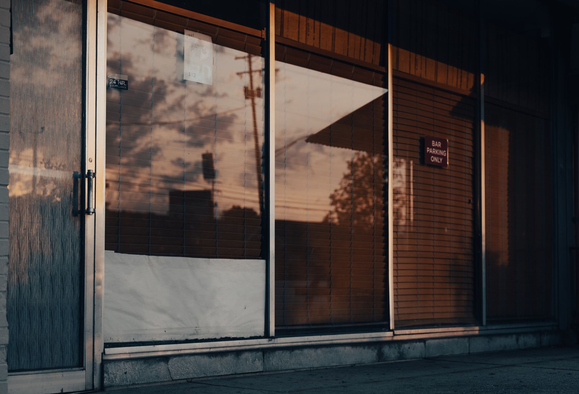 Closed storefront with drawn blinds reflecting a sunset sky