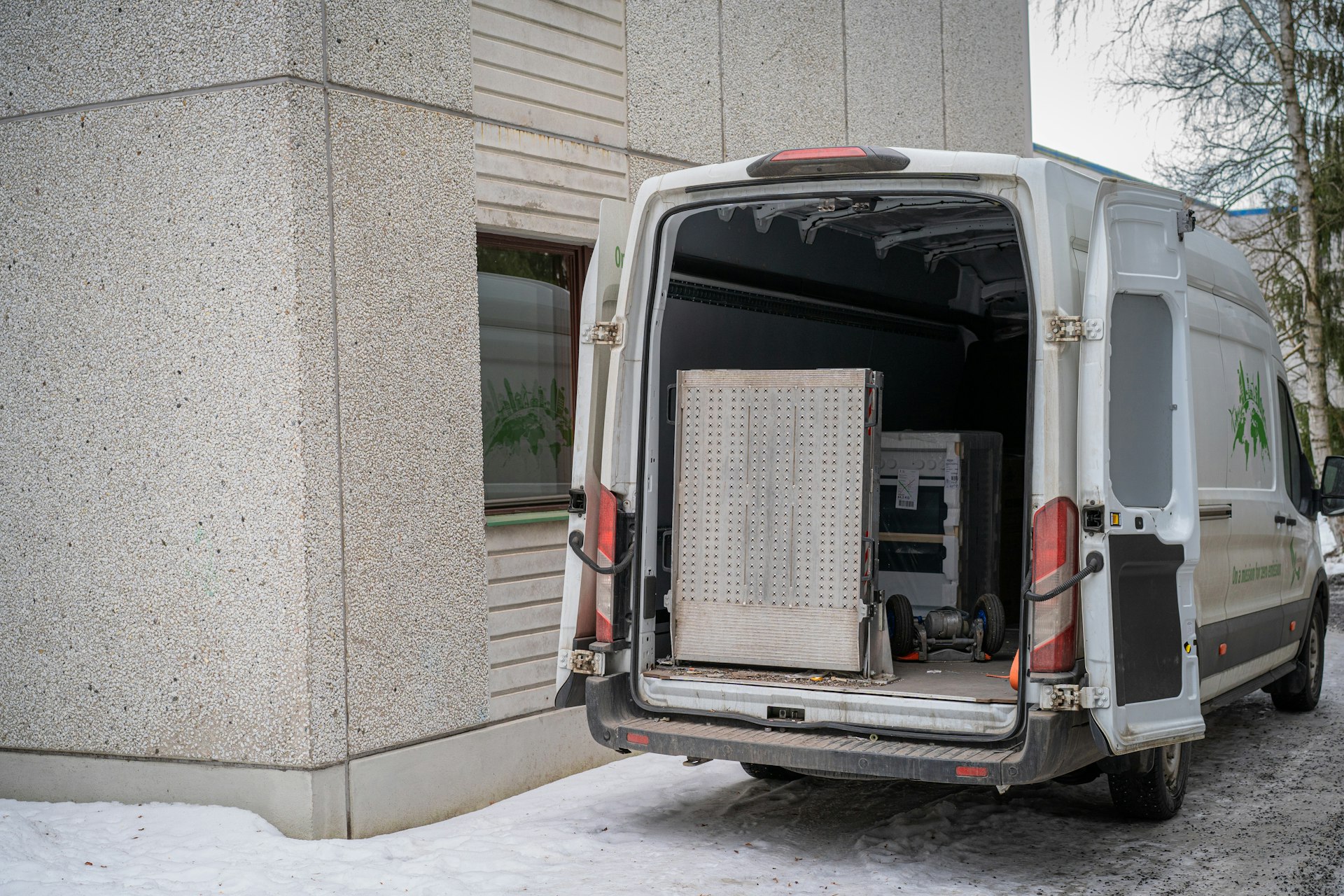 A white cargo van with its rear doors open beside a building in winter