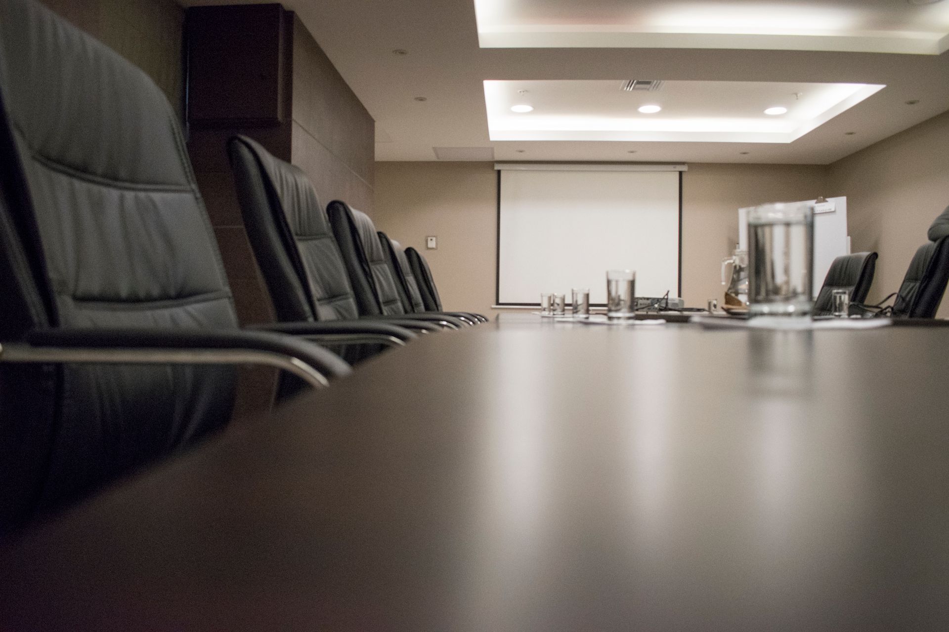 Empty meeting room with a long dark table, leather chairs and a blank projection screen