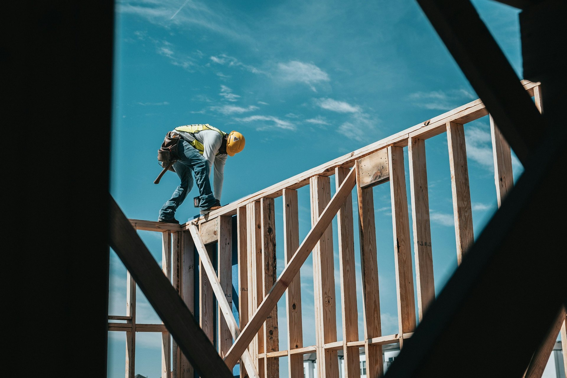 Person in a hard hat and safety vest standing on the wood framing of a house under construction against a blue sky