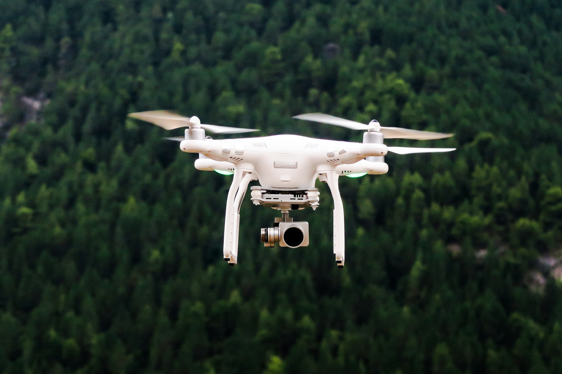 White quadcopter drone flying above a forest