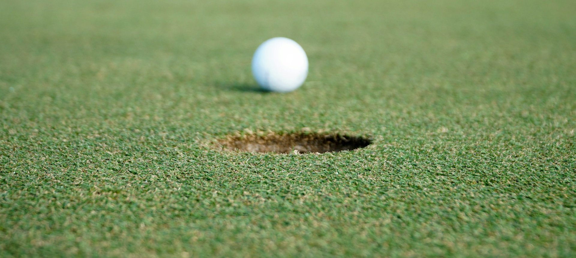 Golf ball resting on a putting green just beside the hole