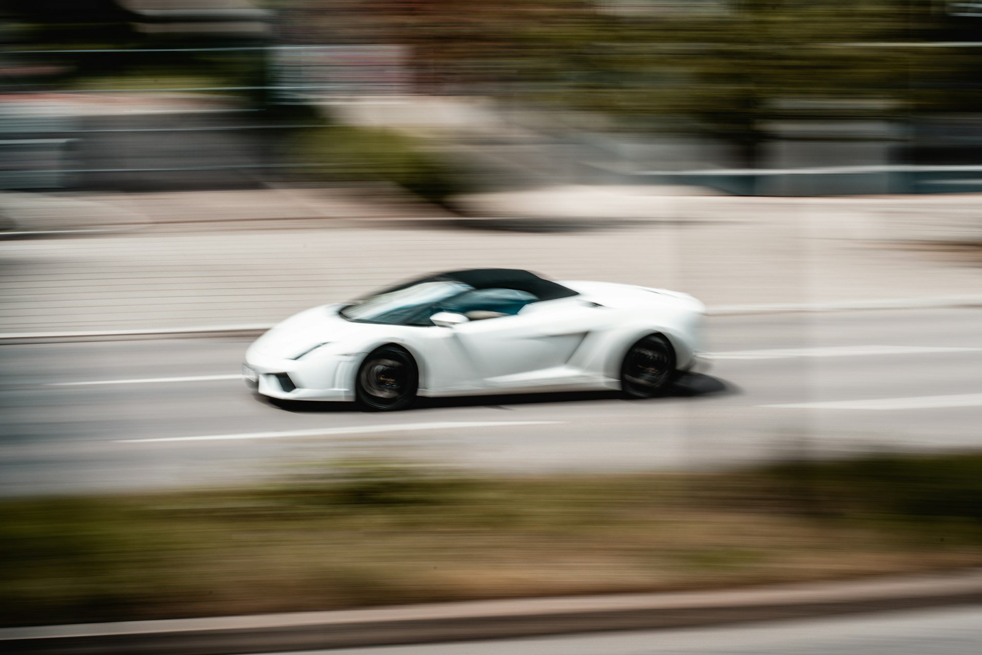 White open-top sports car speeding along a road, blurred by motion