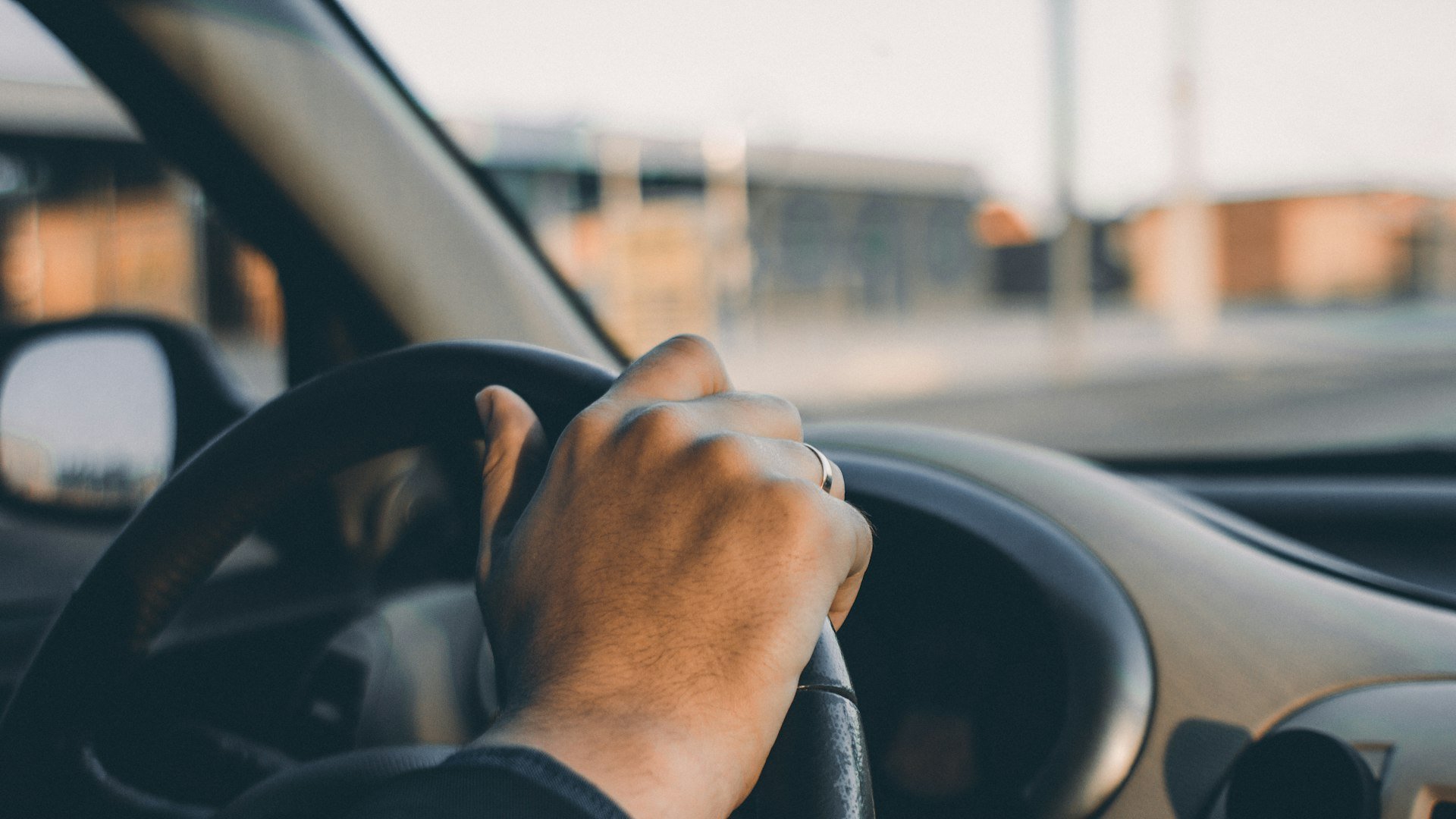 Driver's hand resting on the steering wheel of a car on a street, seen from the passenger side