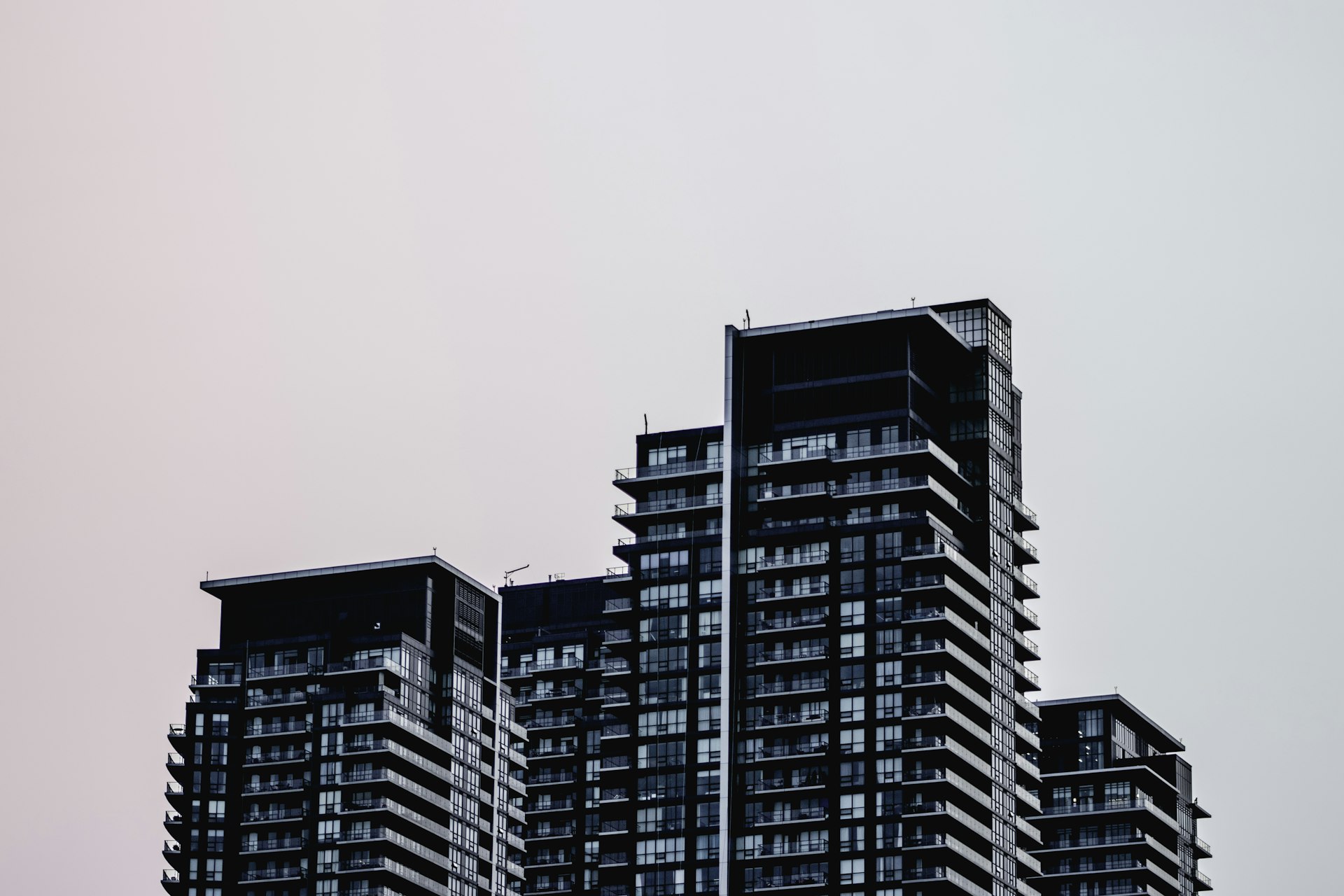 Dark glass condominium towers with stacked balconies against a pale grey sky