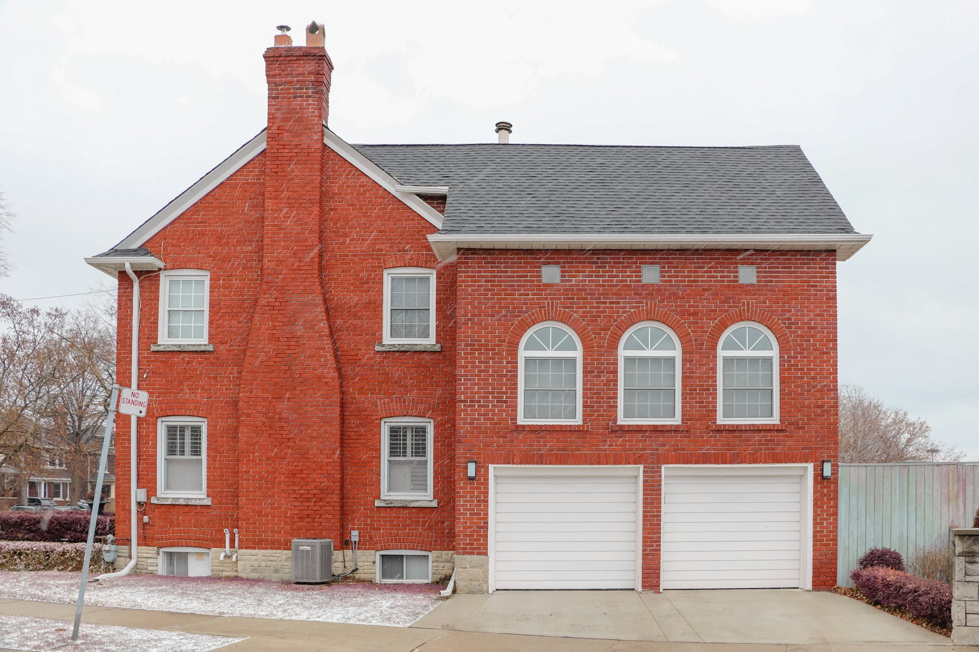 Red-brick two-storey house with a double garage and arched windows on a snowy day