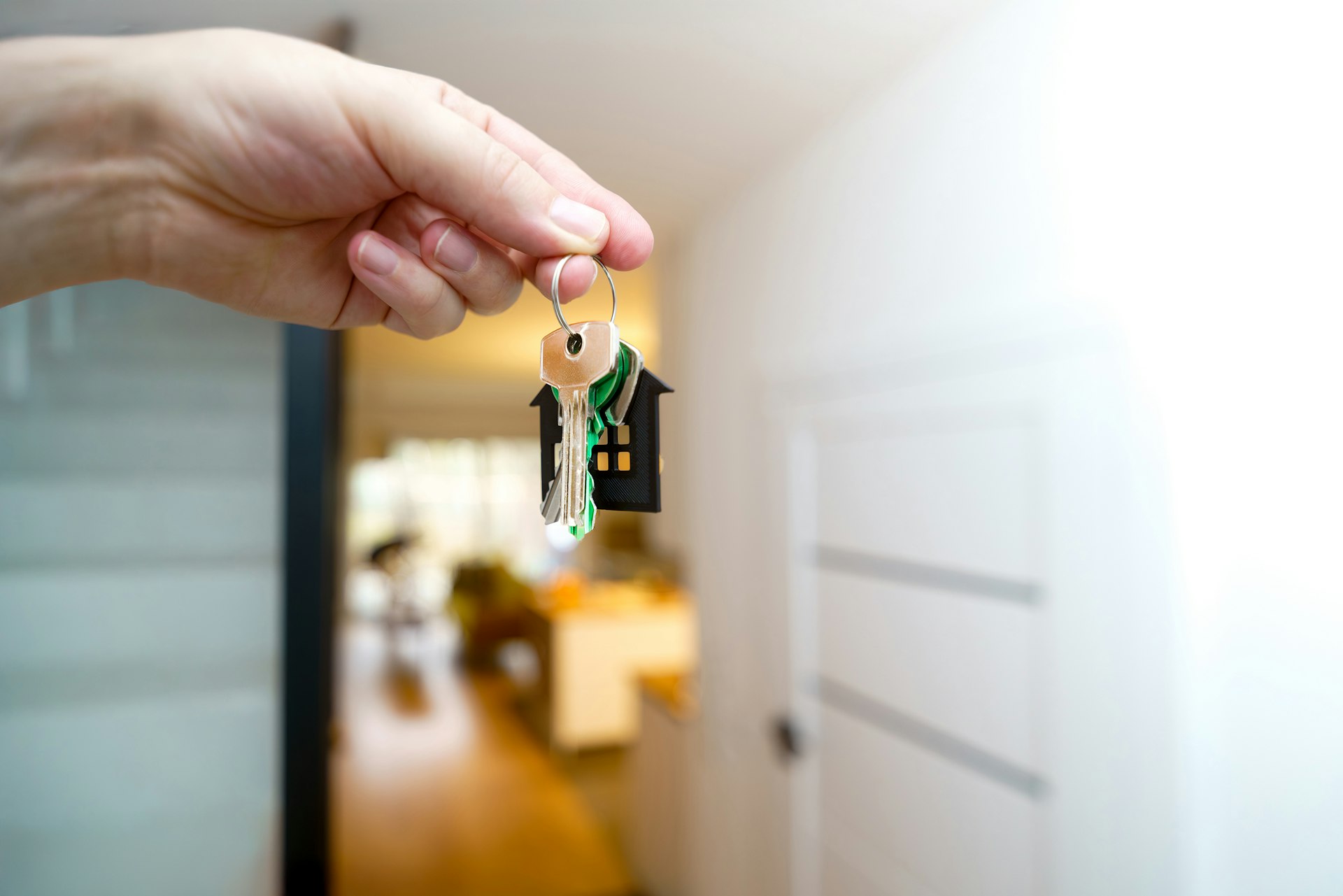 Hand holding out house keys at the entrance to a home