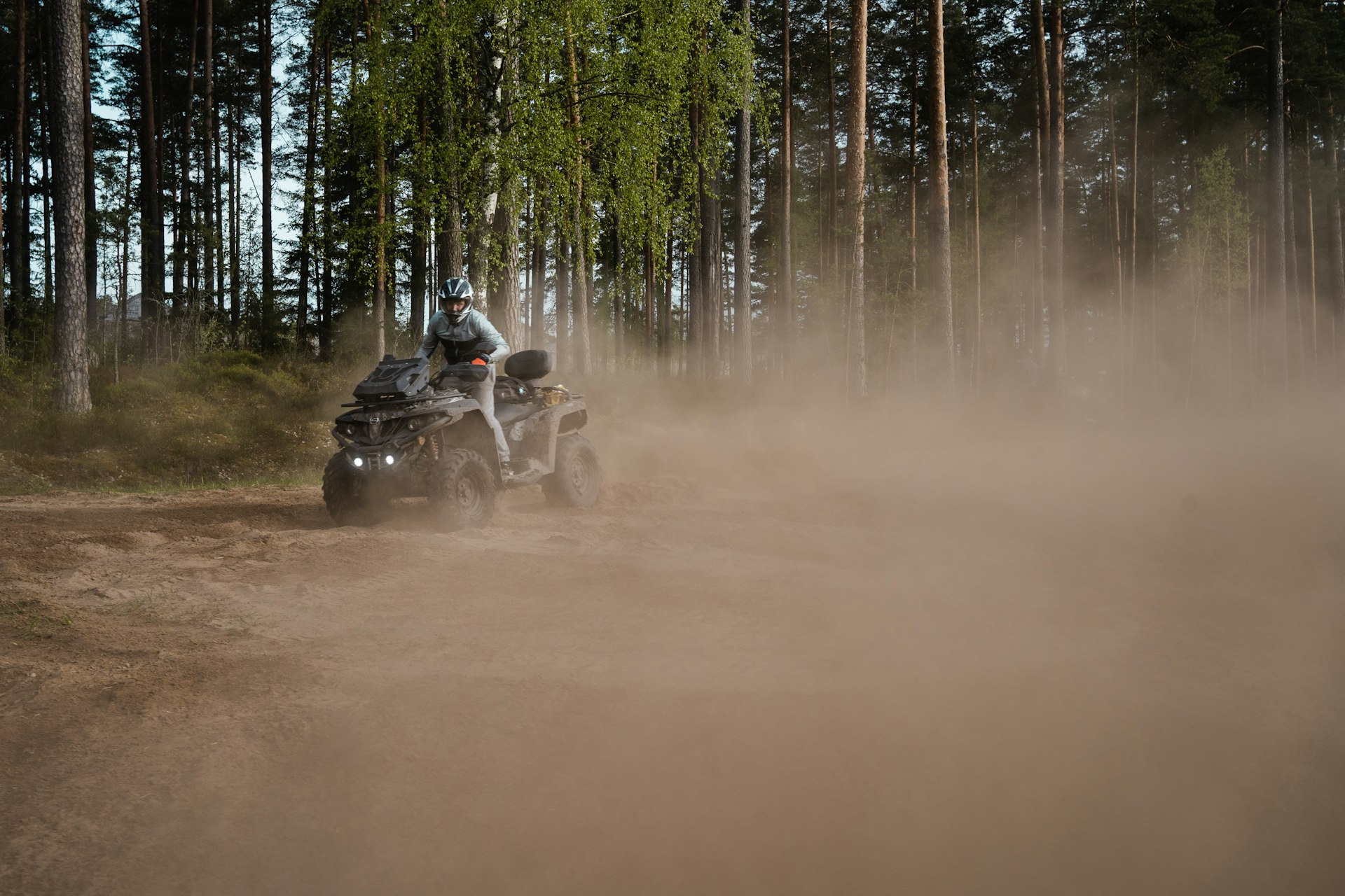 Helmeted rider on an ATV on a dusty forest trail