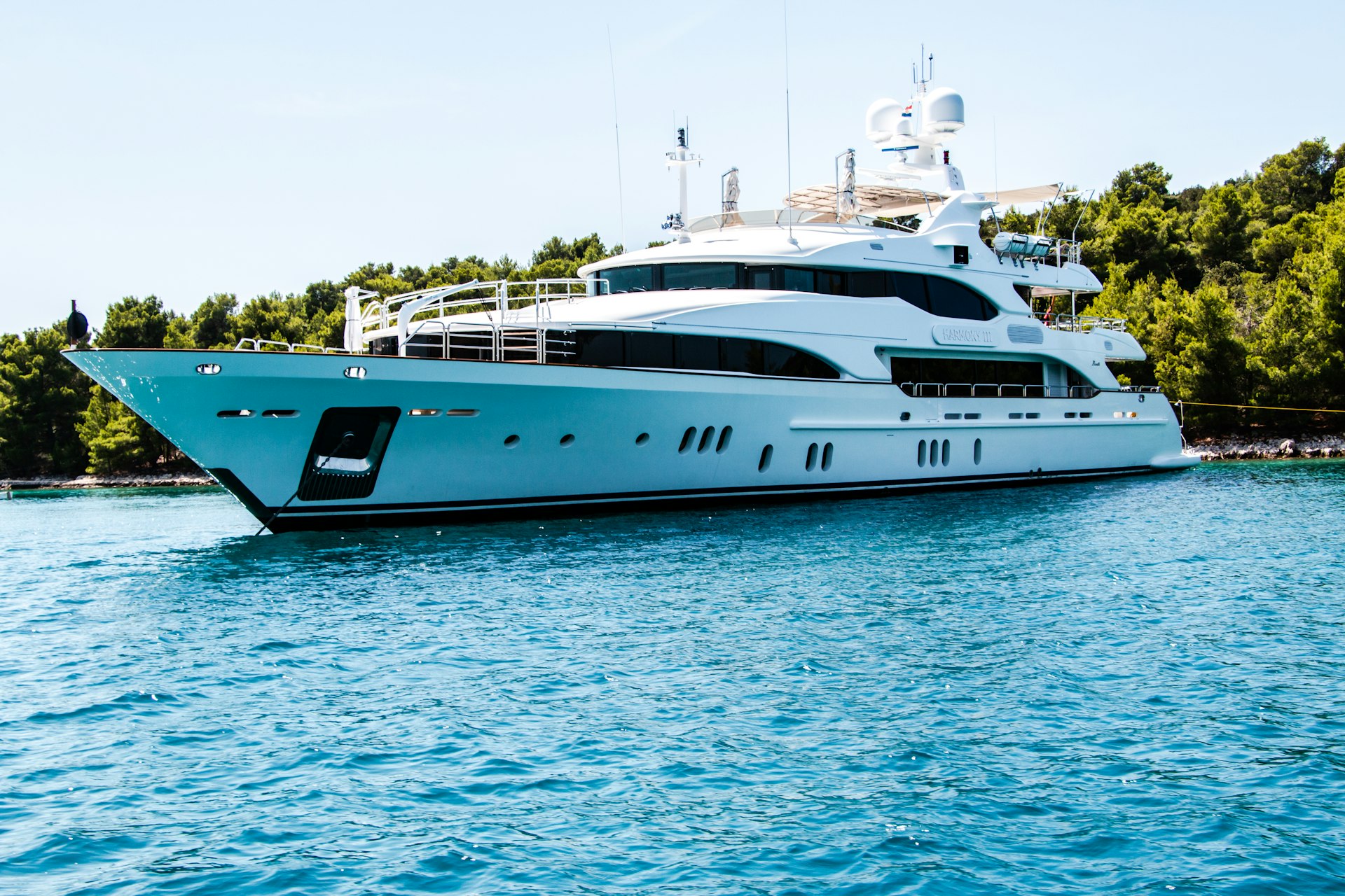 Large white motor yacht anchored off a wooded shoreline