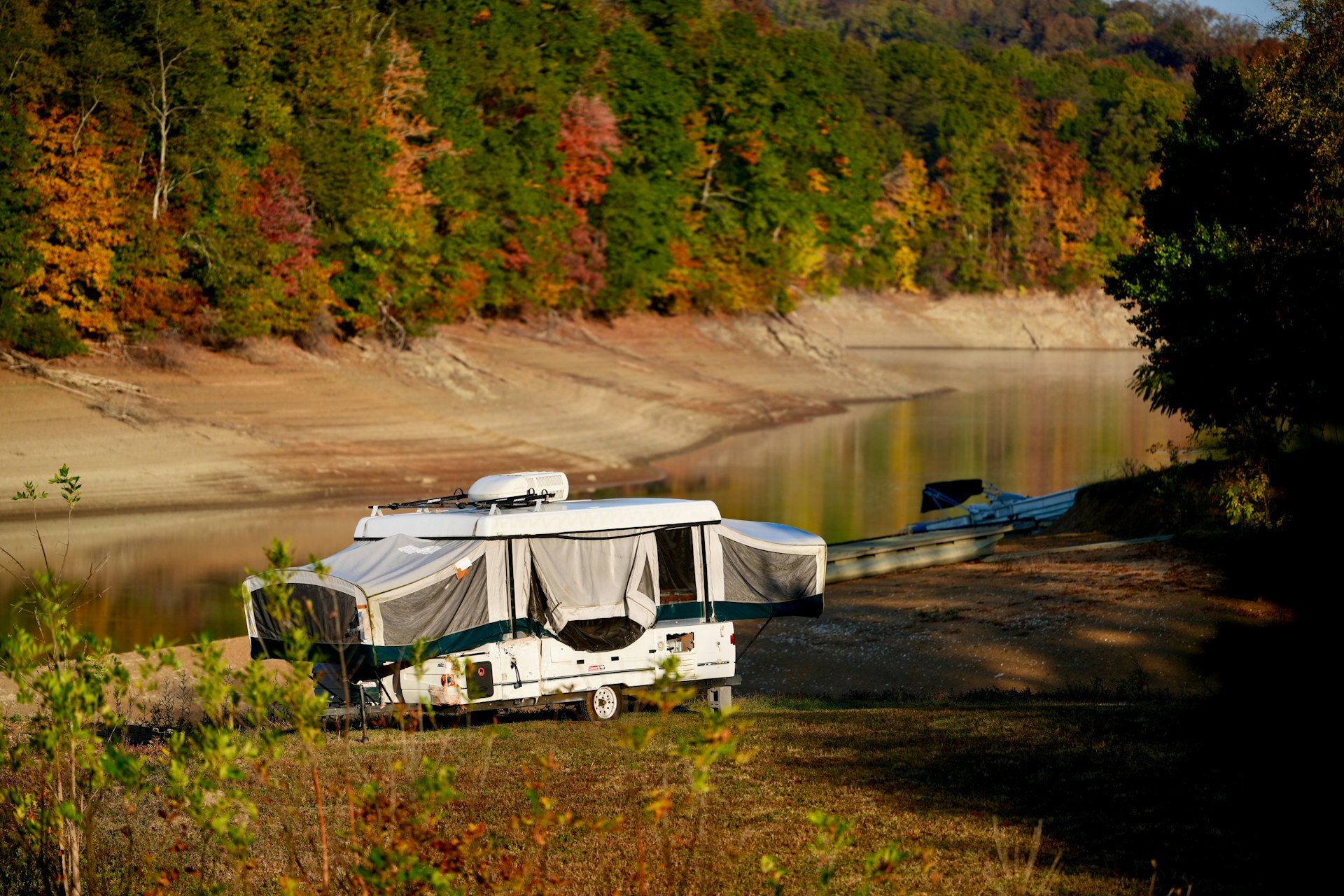 Pop-up camper trailer beside a lake with autumn foliage